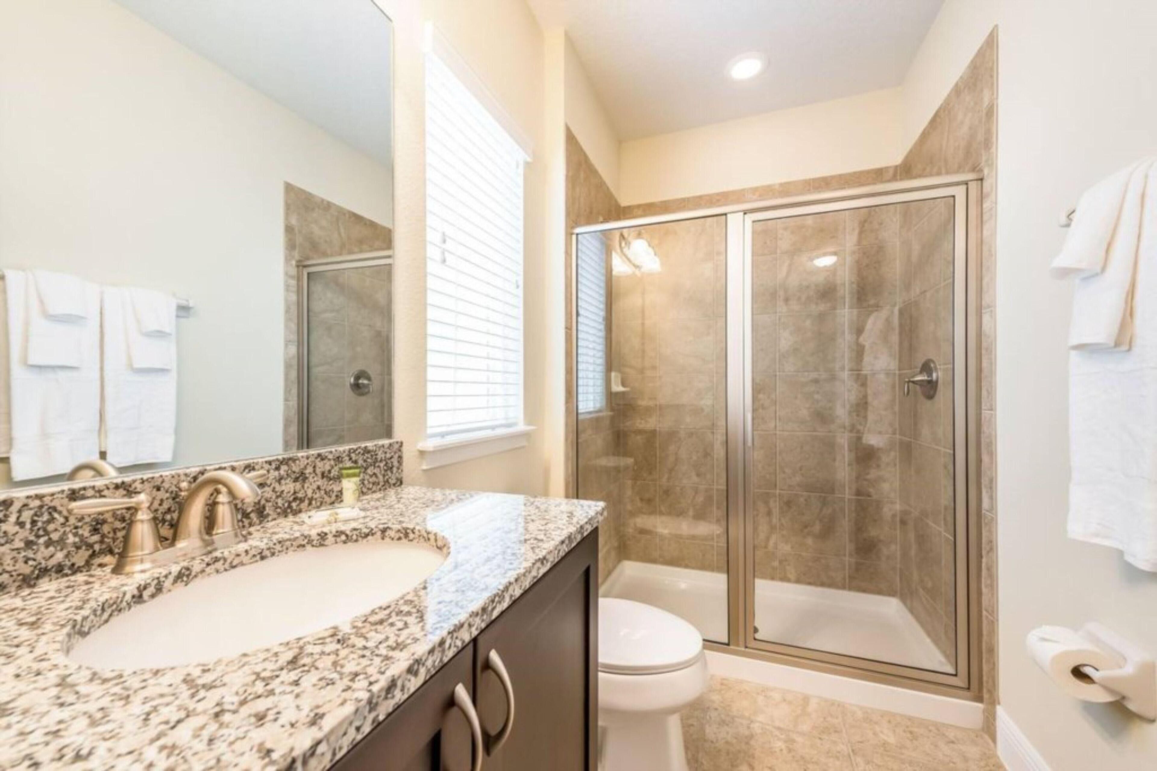 A bathroom with a granite countertop sink, a toilet, and a glass-enclosed shower.