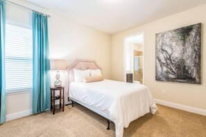 A bedroom with a bed, a nightstand, a lamp, a window with curtains, and a painting on the wall. - Refurbished Lux 6 Bed Golf Views at Reunion Resort by Shine Villas (Kissimmee)