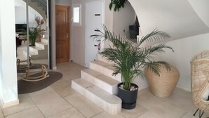 Een modern interieur met een trap naar een vide, een potplant en een rieten stoel.