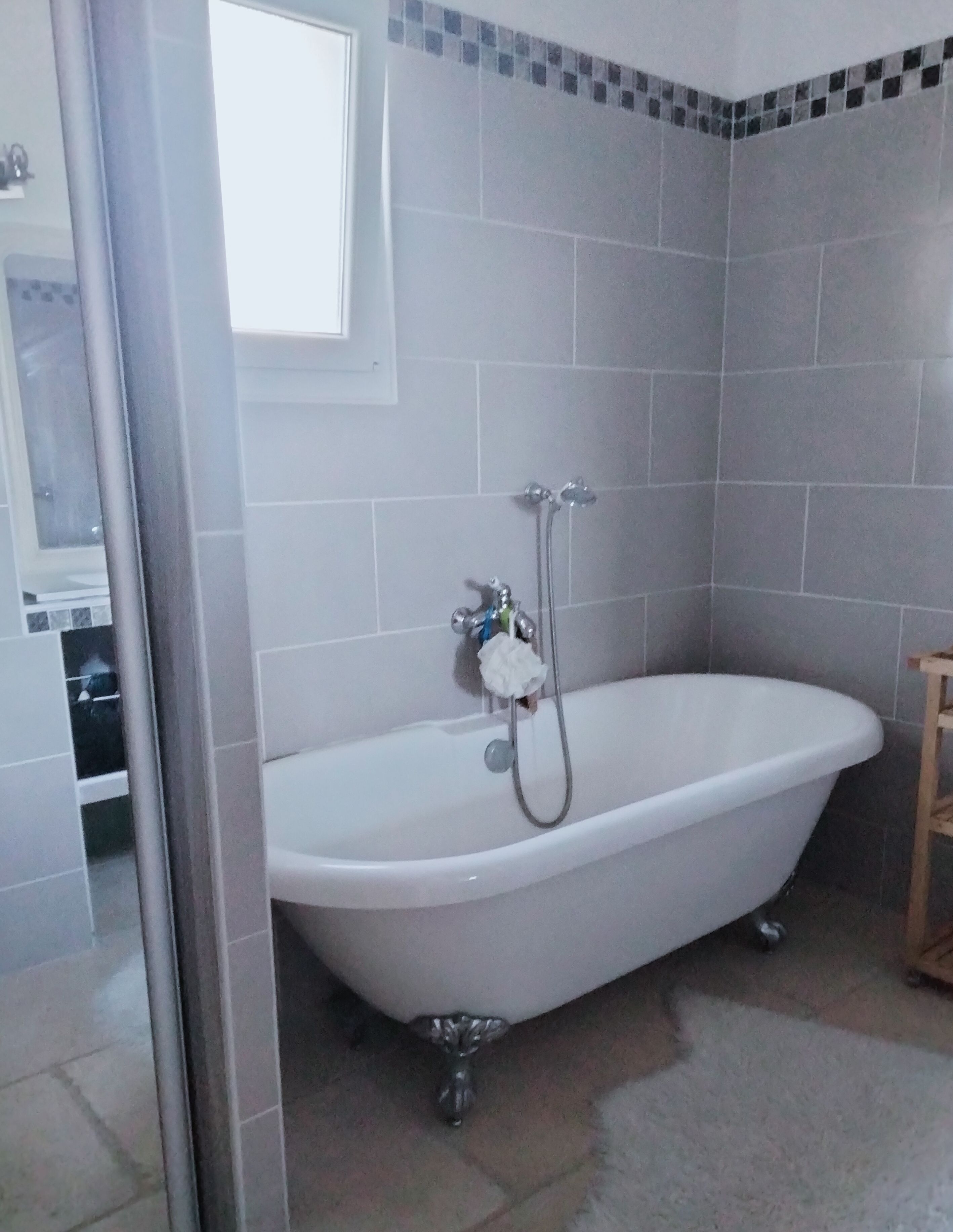 Une salle de bain avec une baignoire sur pieds, une pomme de douche et un carrelage au sol.