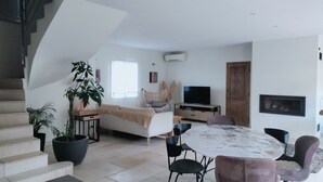 Een moderne woonkamer met een bank, eettafel, stoelen, een trap en een televisie.