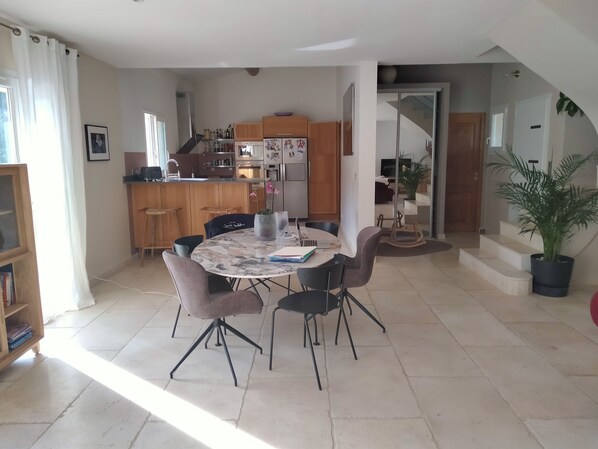 A dining area with a round table, chairs, and a kitchen in the background.