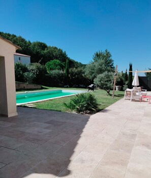 A backyard with a swimming pool, a patio area with outdoor furniture, and a garden with various plants.