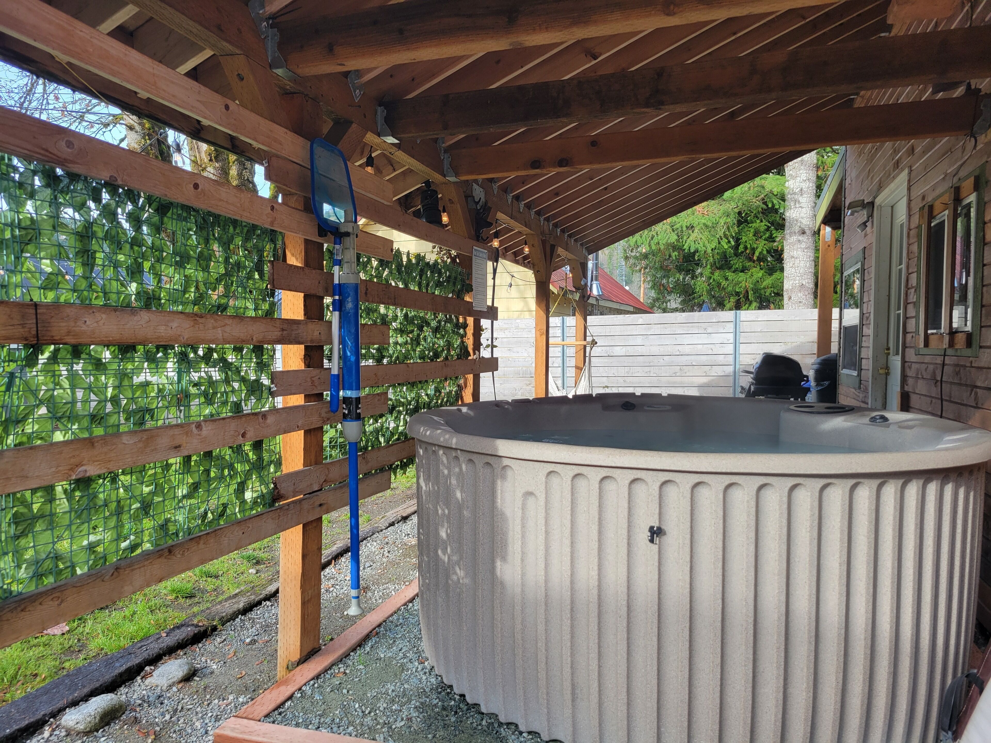 Et boblebad under et træbeklædt pergola med et hegn af metal og grønt i baggrunden.