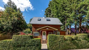 Eine Holzhütte mit Metallbedachung, umgeben von gepflegten Hecken und hohen Bäumen.