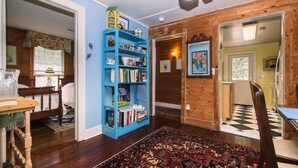 A room with a wooden floor, a blue bookshelf, a patterned rug, and a dining area with a chair and table. - Secluded Hideaway w/ Private Deep Water Dock; Sunrise Views; Kayaker's Paradise (Edisto Island)