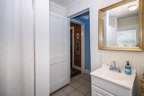 Un baño con lavamanos blanco, espejo con marco dorado y jabón para manos.