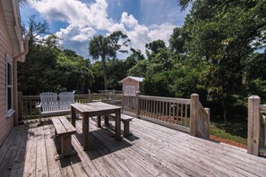 Una terraza de madera con una mesa y sillas, rodeada por un cerco de madera y abundante vegetación.