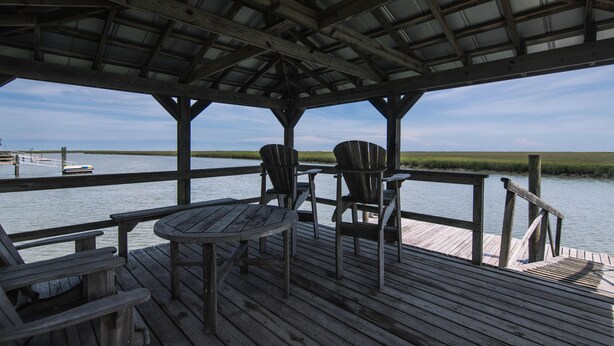 A wooden deck with a covered area, chairs, and a table overlooking a body of water. - Secluded Hideaway w/ Private Deep Water Dock; Sunrise Views; Kayaker's Paradise (Edisto Island)
