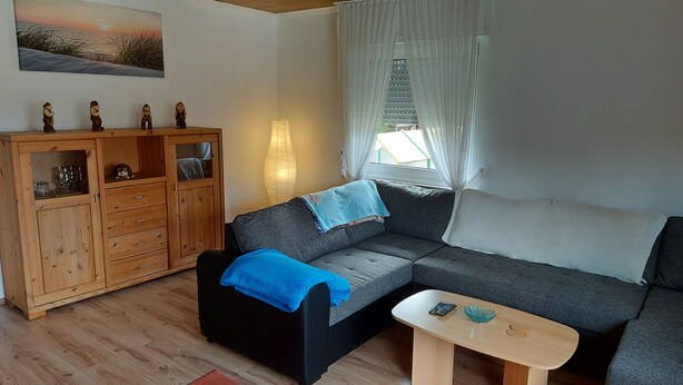 Ein Wohnzimmer mit einem Ecksofa, einem Holzschrank, einer Lampe und einem Gemälde an der Wand.