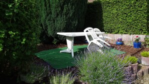 Ein Garten mit einer weißen Sitzgelegenheit im Freien, einer grünen Rasenfläche und verschiedenen Pflanzen, darunter Lavendel.