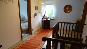 Ein Flur mit Holzbalkon, Teppichboden und einem Bett im angrenzenden Zimmer, sowie ein Fenster mit Vorhängen.