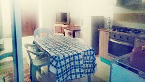 Een kleine keuken met een tafel, stoelen, een televisie, een koelkast en een fornuis.