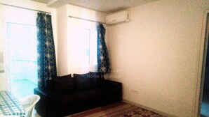 Een woonkamer met een bank, een kamerkleed met patroon, een tafel met geruit tafelkleed, en een raam met gordijnen.