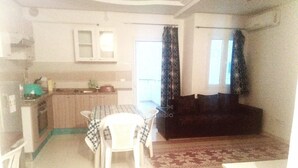 Een ruimtelijk ingerichte leefruimte met kitchenette, een eethoek met tafel en stoelen, en een slaapbank.