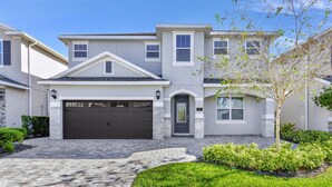 A two-story residential house with a garage, a well-maintained lawn, and a tree in the front yard. - Stylish Home near Disney: Themed Rooms, Game Room & Waterpark - 267SF (Kissimmee)