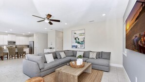 A modern living room with a grey sectional sofa, wooden coffee table, and a ceiling fan. - Stylish Home near Disney: Themed Rooms, Game Room & Waterpark - 267SF (Kissimmee)