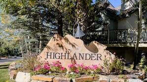 En stenskilte med navnet 'HIGHLANDER' omgivet af en have med lyserøde blomster og en lygtepæl.