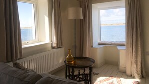 A room with a bed, a small table with a lamp, and a view of the sea through a window. - Waterside (Ravenglass)