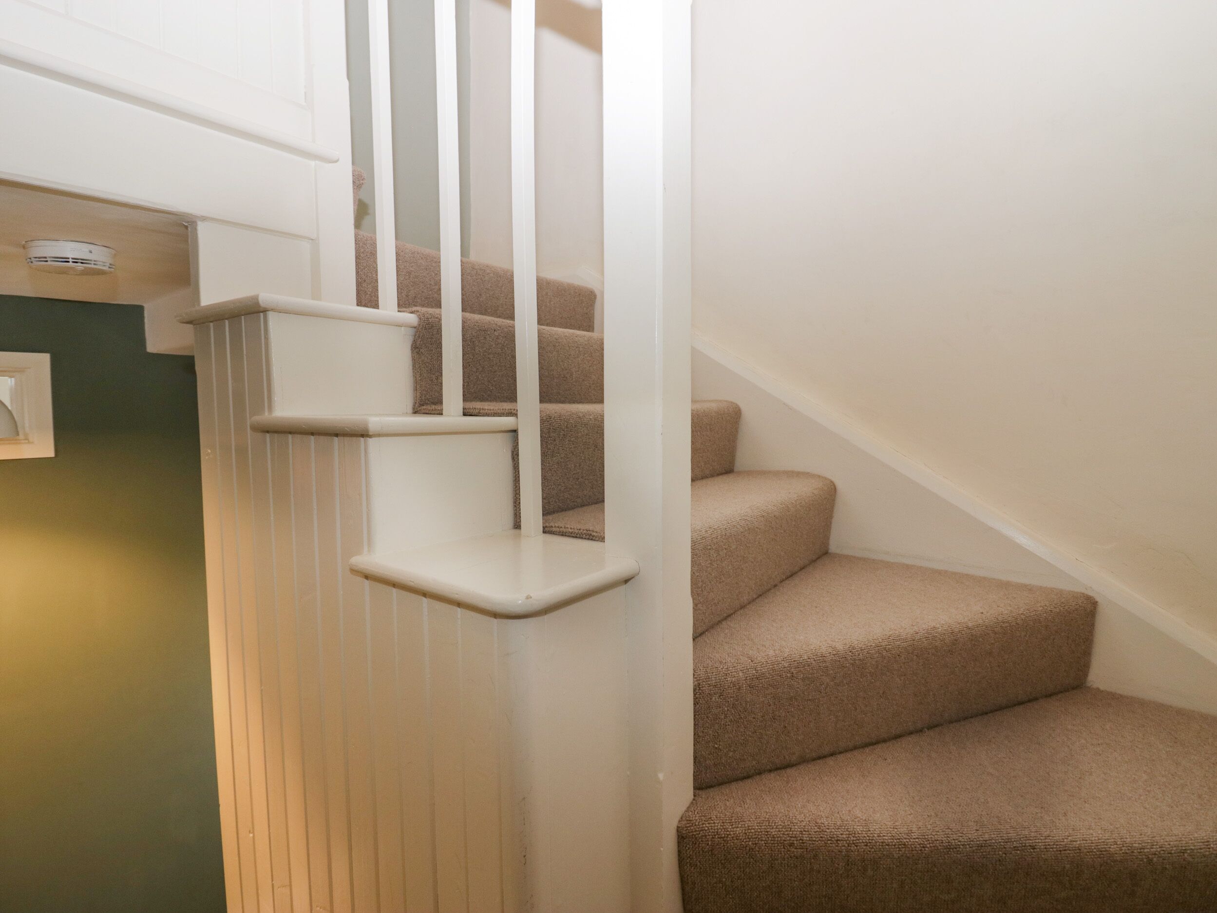 Un escalier avec des rampes blanches et des marches recouvertes d’une moquette beige.