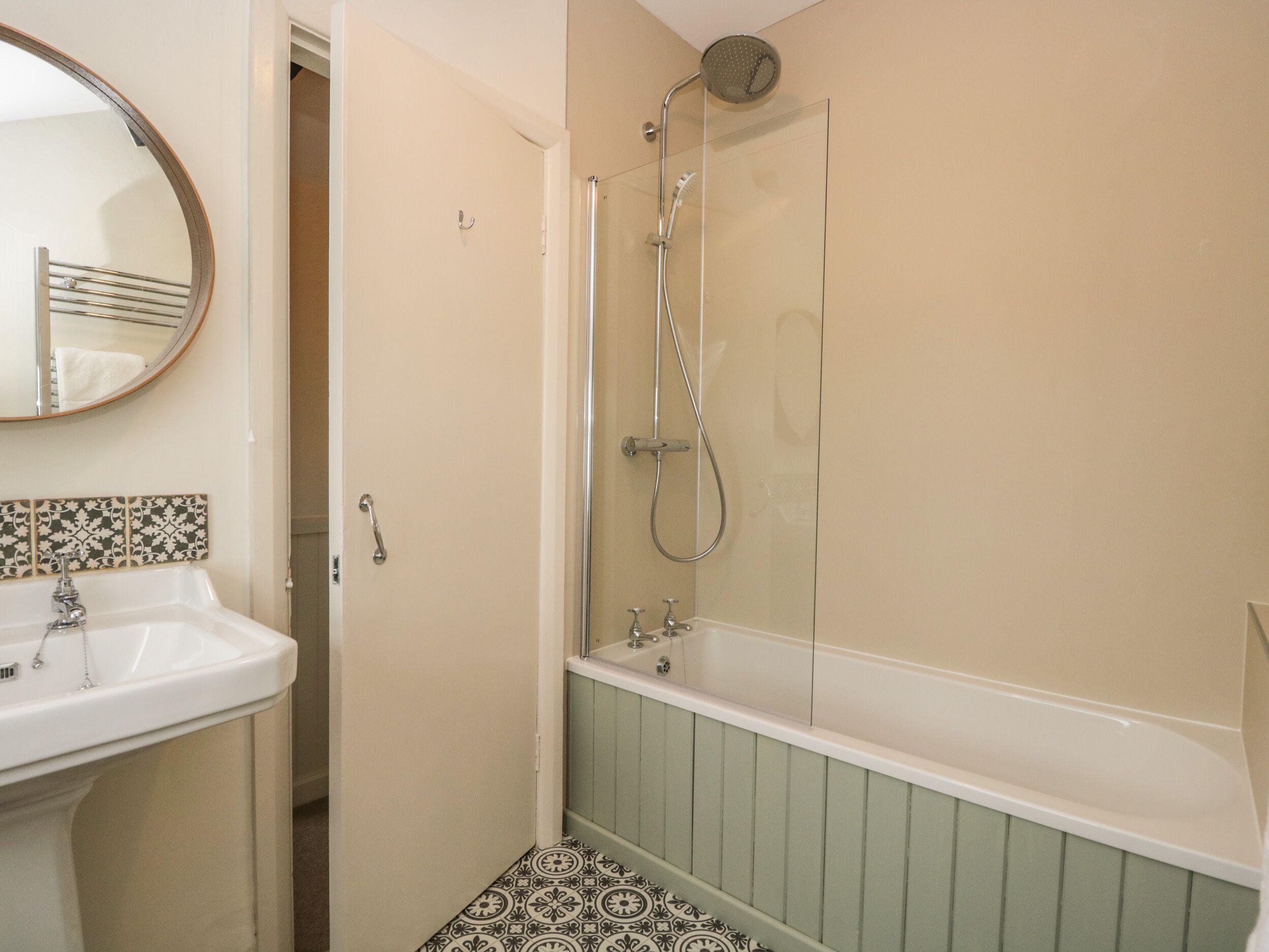 A bathroom with a sink, mirror, shower, and patterned floor tiles.