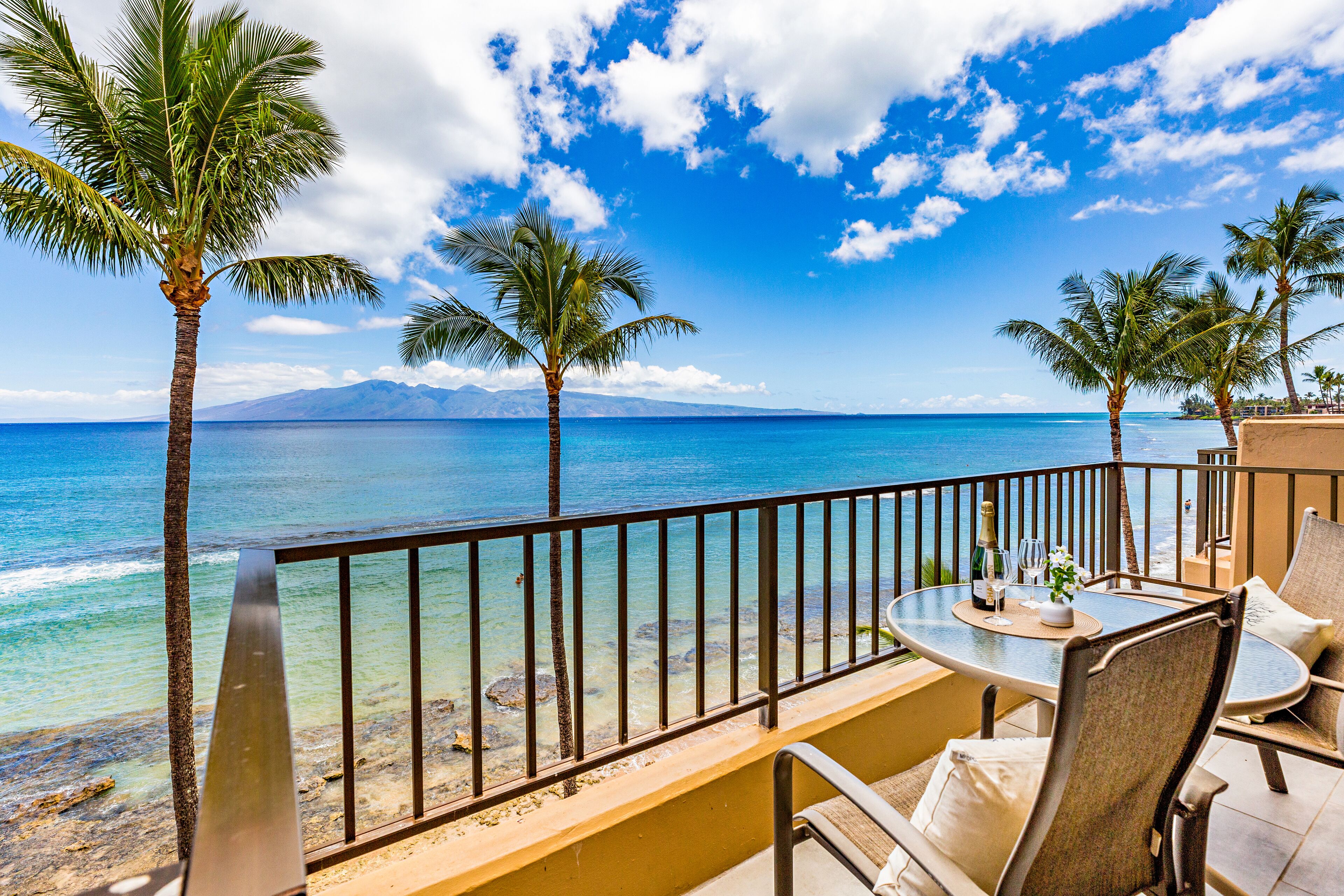 Ein Balkon mit Tisch, Stühlen und Blick auf das Meer und die Berge.