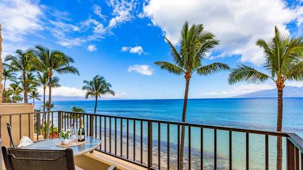 Un balcone con tavolo, sedie e vista sull'oceano e palme.