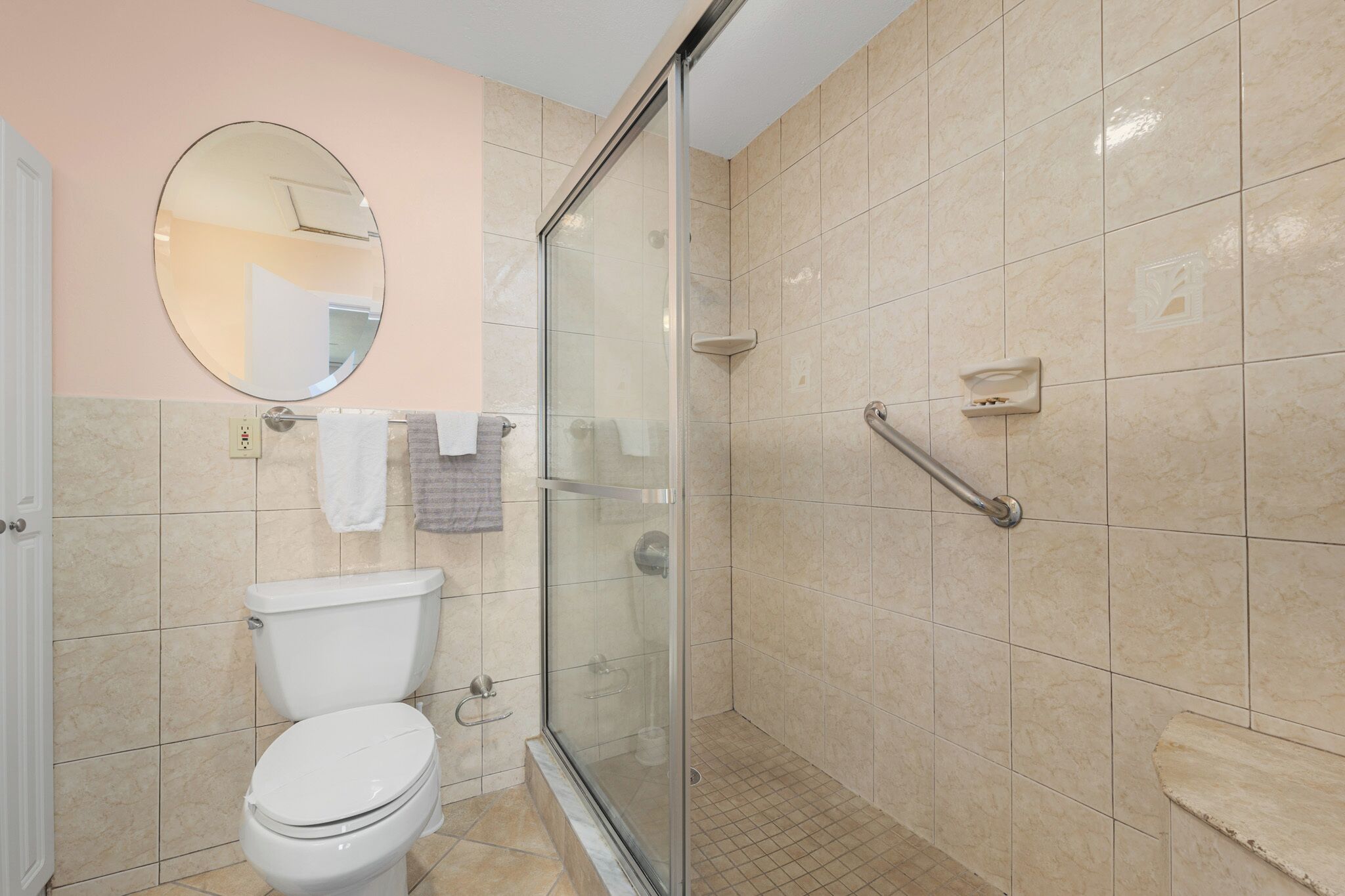A bathroom with a toilet, a glass-enclosed shower, a round mirror, and a towel rack.