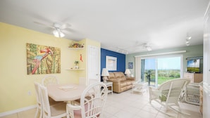 A dining area with a table and chairs, a sofa, and a view through a glass door. - Four Winds by Distinctive Beach Rentals (St. Augustine)