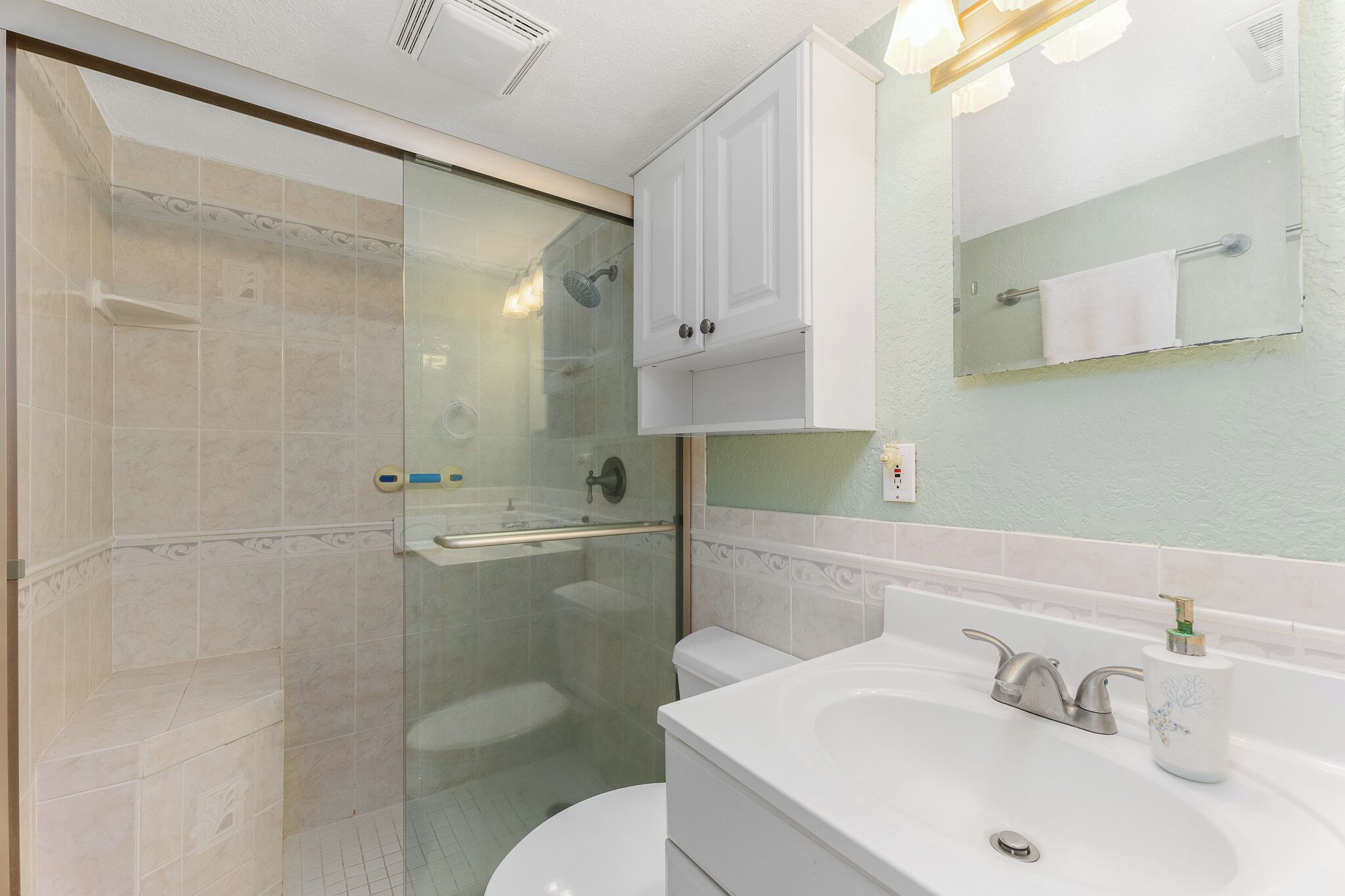 A modern bathroom with a glass-enclosed shower, a white sink with a soap dispenser, and a mirror above the sink.