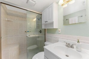Un baño moderno con ducha de vidrio, un lavabo blanco con dispensador de jabón y un espejo sobre el lavabo.