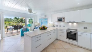 A modern kitchen with white cabinetry, a built-in oven, and a large island with a sink. - Beachside apartment - Glitter Bay Estate 309 (1 bed) (Porters)