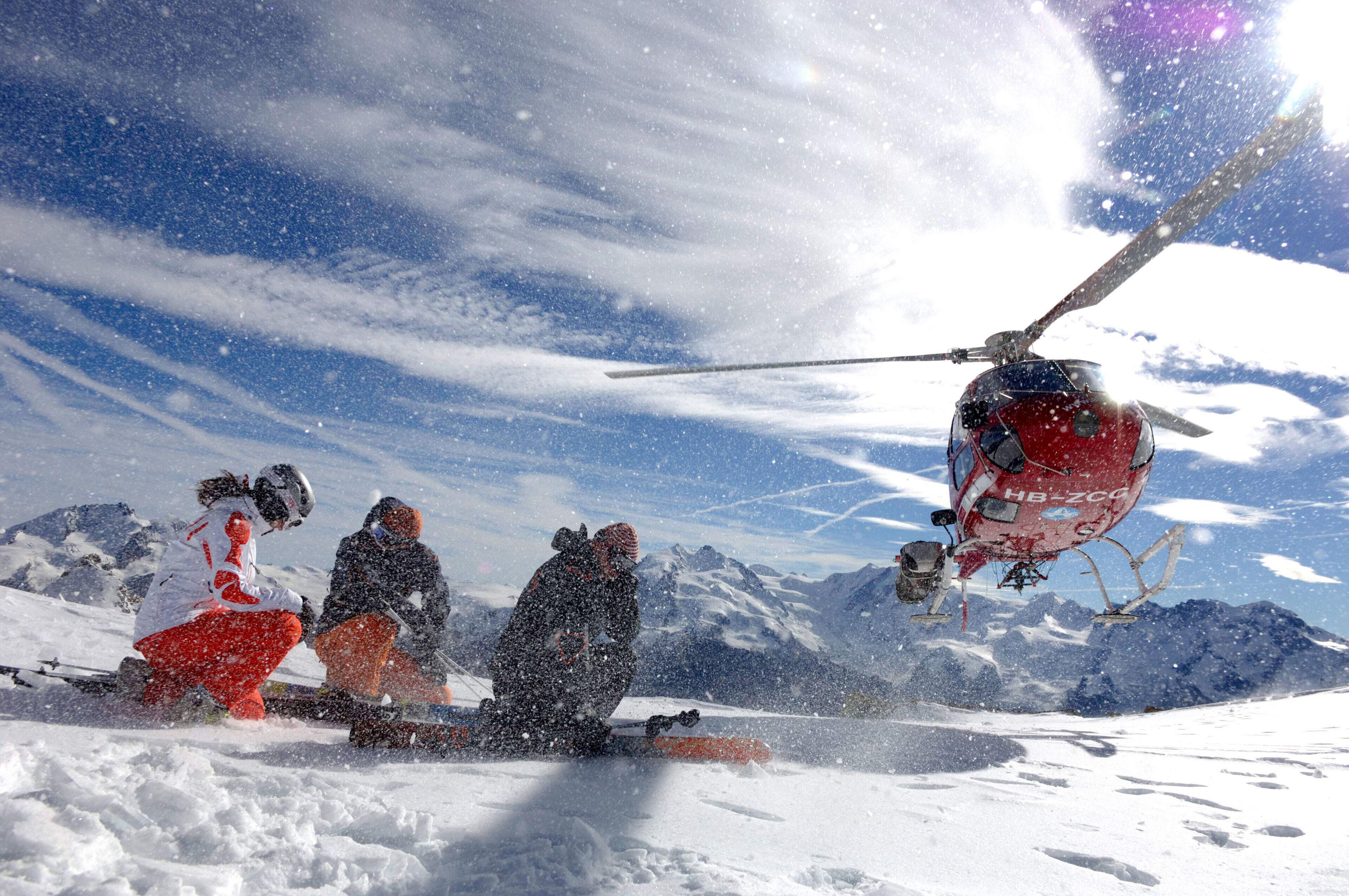A group of people on a snowy mountain with a helicopter in the background.