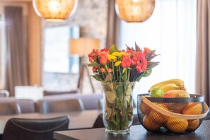Ruokailutila, jossa on kahdelle katettu pöytä, maljakko täynnä kukkia ja hedelmäkori.