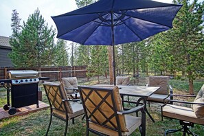 An outdoor patio with a table and chairs, a grill, and an umbrella.