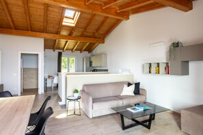 A modern interior with a wooden ceiling, a sofa, a glass coffee table, and a kitchen area. - Le Casette - Gargnà with pool and lake view (Toscolano-Maderno)