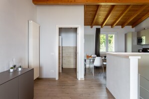 A modern kitchen with a wooden ceiling, a dining area with a table and chairs, and a view of greenery outside. - Le Casette - Gargnà with pool and lake view (Toscolano-Maderno)