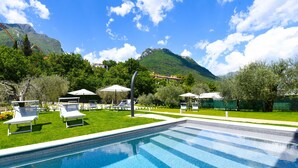 A swimming pool with lounge chairs and umbrellas, surrounded by greenery and mountains in the background. - Le Casette - Leccino with lake view, pool and private Jacuzzi (Toscolano-Maderno)