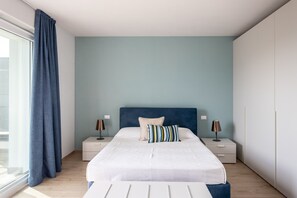 Quarto com cama, duas mesas de cabeceira, janela com cortinas e parede azul claro.