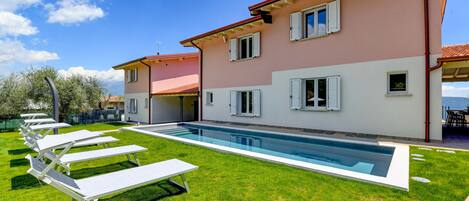 A two-story house with a swimming pool, white shutters, and a covered patio area.
