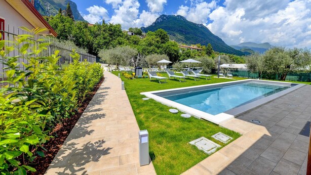 A swimming pool with lounge chairs, a paved walkway, and a mountainous backdrop.