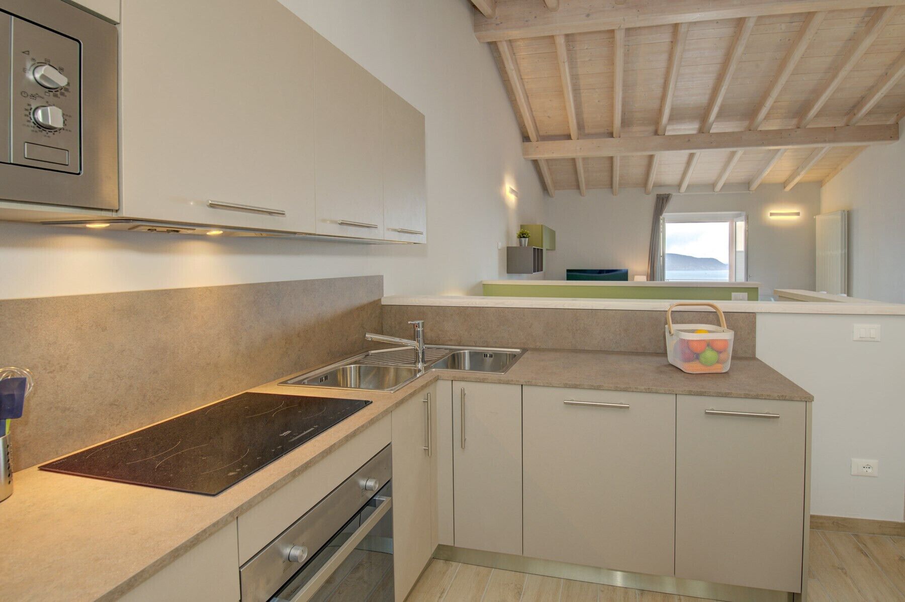 A compact kitchen with a stainless steel sink, a built-in oven, and a wooden ceiling.