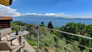 A balcony with a table and chairs overlooking a lake with mountains in the background.