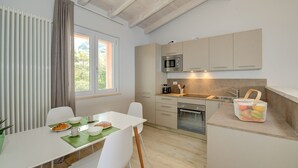 A compact kitchen with a microwave, sink, and cabinets. There's a dining table with chairs and a window with curtains.