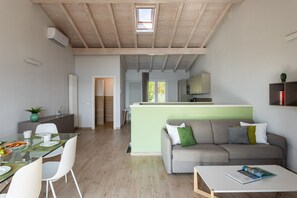 A modern living room with a sofa, a dining table with chairs, and a kitchen area in the background. - Le Casette - Casaliva with pool and lake view (Toscolano-Maderno)