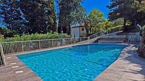 A rectangular swimming pool with clear blue water, surrounded by a tiled deck and a metal fence.