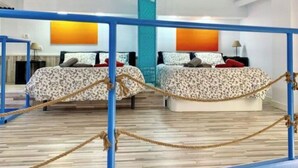 Une chambre d’hôtel avec deux lits, un plancher en bois, une rambarde bleue et une barrière faite de cordes.