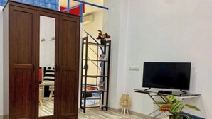 Un salon avec une armoire en bois, un téléviseur posé sur un meuble, une petite table avec une plante et un tapis à motifs.