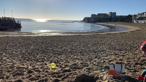 En strand med sandet bredde, en mole og bygninger i baggrunden.