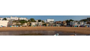 A coastal town with buildings along the beach, a sandy shore, and a few boats.